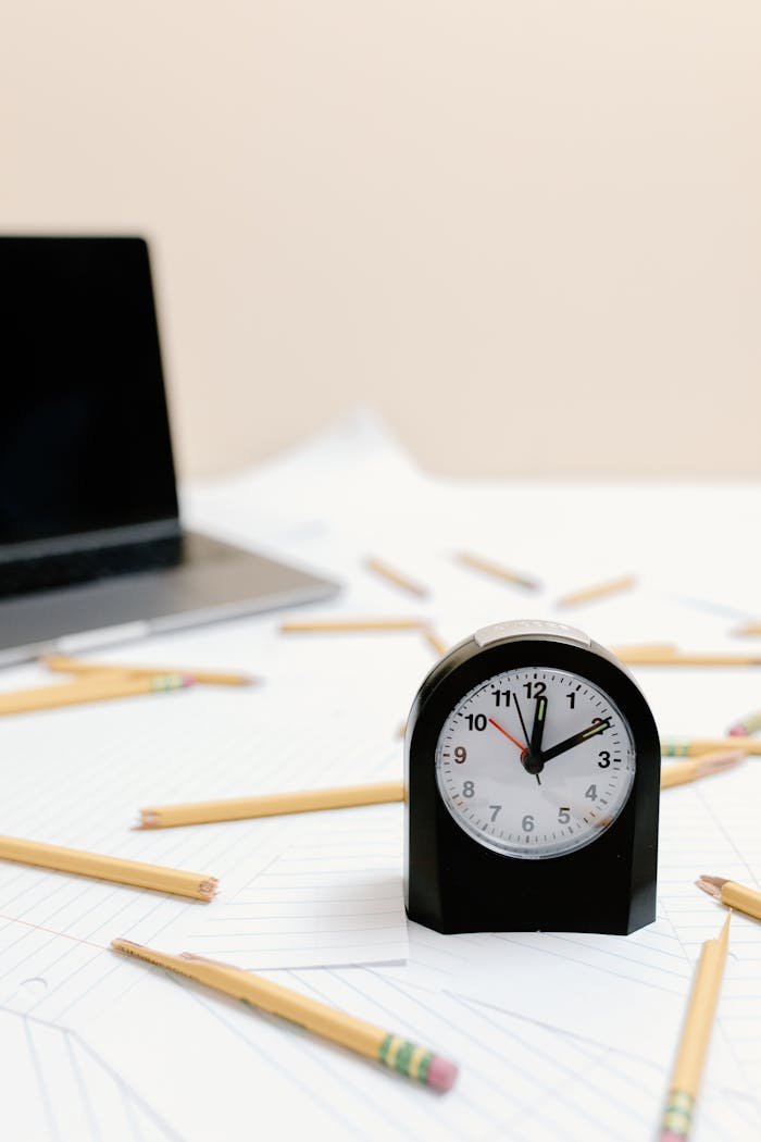 A clock on scattered papers and pencils symbolizes time management and stress.